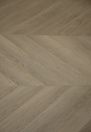 A picture showing the 6.5mm lvp flooring called Saigon in the chevron pattern. This vinyl floor is uniquely crafted and can only be installed in the chevron pattern. It has a light medium beige hue and silver chain embossing, giving the floor an ultra-realistic look.