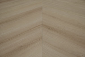 A picture showing the 6.5mm lvp flooring called Pompeii in the chevron pattern. This vinyl floor is uniquely crafted and can only be installed in the chevron pattern. It has a light medium beige hue and silver chain embossing, giving the floor an ultra-realistic look.