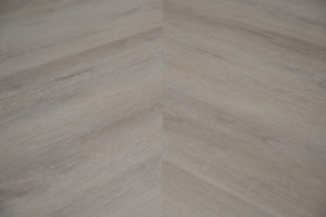 A picture showing the 6.5mm lvp flooring called Mumbai in the chevron pattern. This vinyl floor is uniquely crafted and can only be installed in the chevron pattern. It has a light grey-beige hue and silver chain embossing, giving the floor an ultra-realistic look.