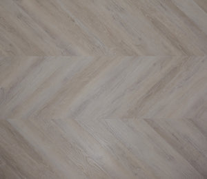 A picture showing the 6.5mm lvp flooring called Mumbai in the chevron pattern. This vinyl floor is uniquely crafted and can only be installed in the chevron pattern. It has a light grey-beige hue and silver chain embossing, giving the floor an ultra-realistic look.