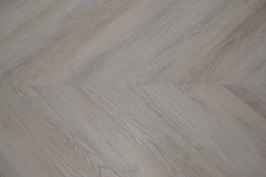 A picture showing the 6.5mm lvp flooring called Mumbai in the chevron pattern. This vinyl floor is uniquely crafted and can only be installed in the chevron pattern. It has a light grey-beige hue and silver chain embossing, giving the floor an ultra-realistic look.