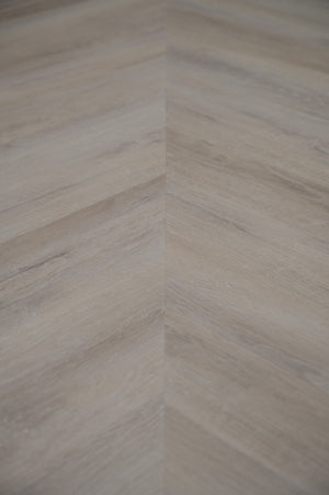 A picture showing the 6.5mm lvp flooring called Mumbai in the chevron pattern. This vinyl floor is uniquely crafted and can only be installed in the chevron pattern. It has a light grey-beige hue and silver chain embossing, giving the floor an ultra-realistic look.