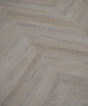 A picture showing the 6.5mm lvp flooring called Mumbai in the chevron pattern. This vinyl floor is uniquely crafted and can only be installed in the chevron pattern. It has a light grey-beige hue and silver chain embossing, giving the floor an ultra-realistic look.