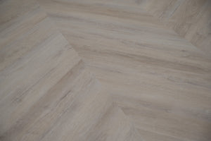 A picture showing the 6.5mm lvp flooring called Mumbai in the chevron pattern. This vinyl floor is uniquely crafted and can only be installed in the chevron pattern. It has a light grey-beige hue and silver chain embossing, giving the floor an ultra-realistic look.