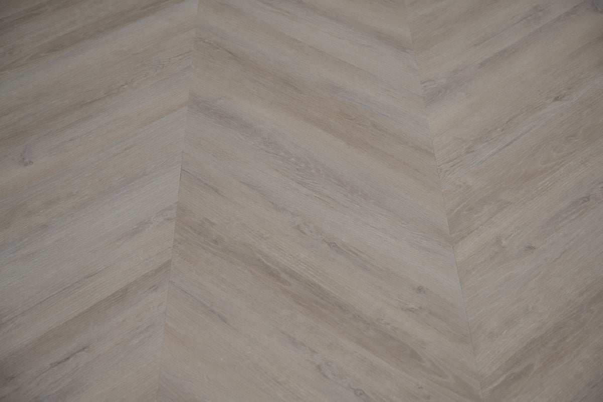 A picture showing the 6.5mm lvp flooring called Mumbai in the chevron pattern. This vinyl floor is uniquely crafted and can only be installed in the chevron pattern. It has a light grey-beige hue and silver chain embossing, giving the floor an ultra-realistic look.