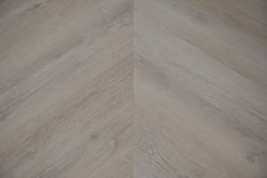 A picture showing the 6.5mm lvp flooring called Mumbai in the chevron pattern. This vinyl floor is uniquely crafted and can only be installed in the chevron pattern. It has a light grey-beige hue and silver chain embossing, giving the floor an ultra-realistic look.