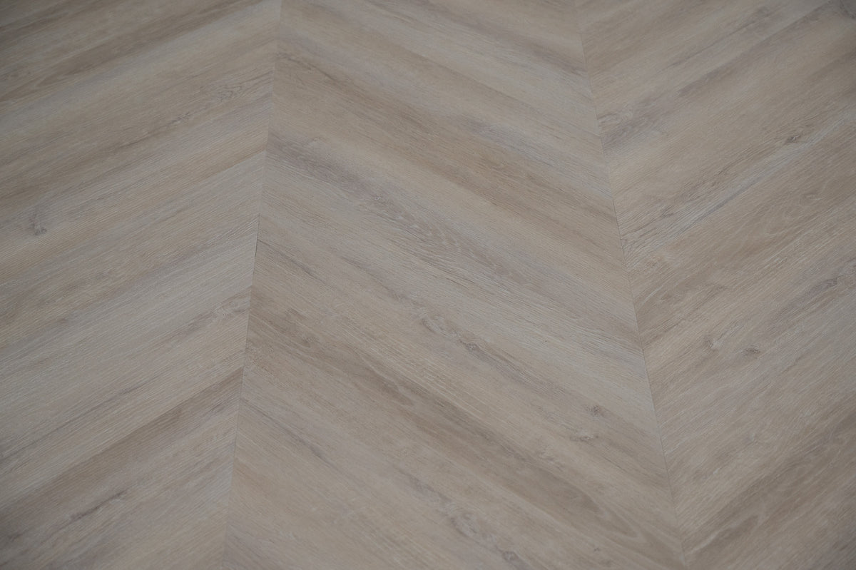 A picture showing the 6.5mm lvp flooring called Mumbai in the chevron pattern. This vinyl floor is uniquely crafted and can only be installed in the chevron pattern. It has a light grey-beige hue and silver chain embossing, giving the floor an ultra-realistic look.