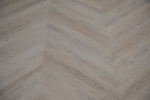 A picture showing the 6.5mm lvp flooring called Mumbai in the chevron pattern. This vinyl floor is uniquely crafted and can only be installed in the chevron pattern. It has a light grey-beige hue and silver chain embossing, giving the floor an ultra-realistic look.