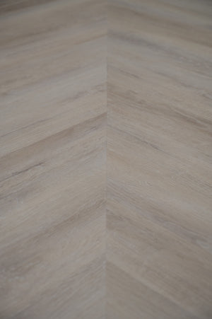 A picture showing the 6.5mm lvp flooring called Mumbai in the chevron pattern. This vinyl floor is uniquely crafted and can only be installed in the chevron pattern. It has a light grey-beige hue and silver chain embossing, giving the floor an ultra-realistic look.