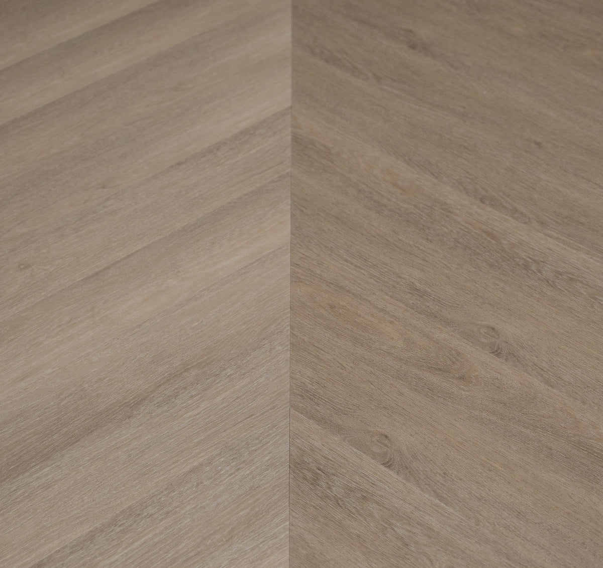 A picture showing the 6.5mm lvp flooring called Saigon in the chevron pattern. This vinyl floor is uniquely crafted and can only be installed in the chevron pattern. It has a light medium beige hue and silver chain embossing, giving the floor an ultra-realistic look.