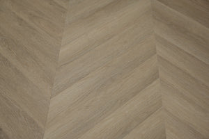 A picture showing the 6.5mm lvp flooring called Saigon in the chevron pattern. This vinyl floor is uniquely crafted and can only be installed in the chevron pattern. It has a light medium beige hue and silver chain embossing, giving the floor an ultra-realistic look.