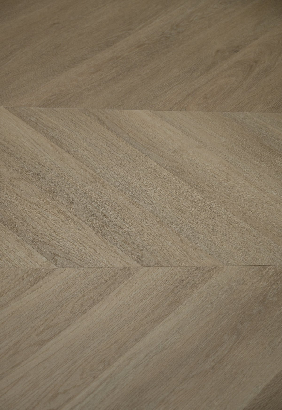 A picture showing the 6.5mm lvp flooring called Saigon in the chevron pattern. This vinyl floor is uniquely crafted and can only be installed in the chevron pattern. It has a light medium beige hue and silver chain embossing, giving the floor an ultra-realistic look.