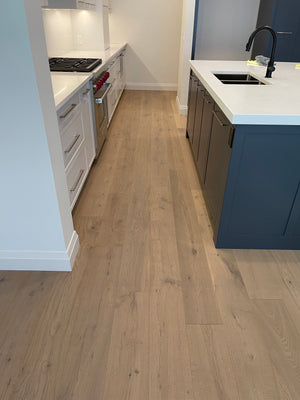 A picture of Istanbul oak hardwood installed in the kitchen of a newly built home. The kitchen is bright and modern, with painted wood accent cabinets that compliment the colour of the floor. There is lots of natural light present.