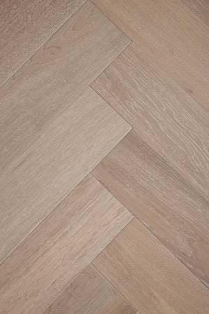 A photo showing Niagara herringbone oak hardwood from the Wildwood Nature Herringbone Collection. This hardwood has a very light grey-beige color with some white washing that accentuates the grain of the white oak. There is little to no variation and knotting in this wood, characteristic of its high grade.