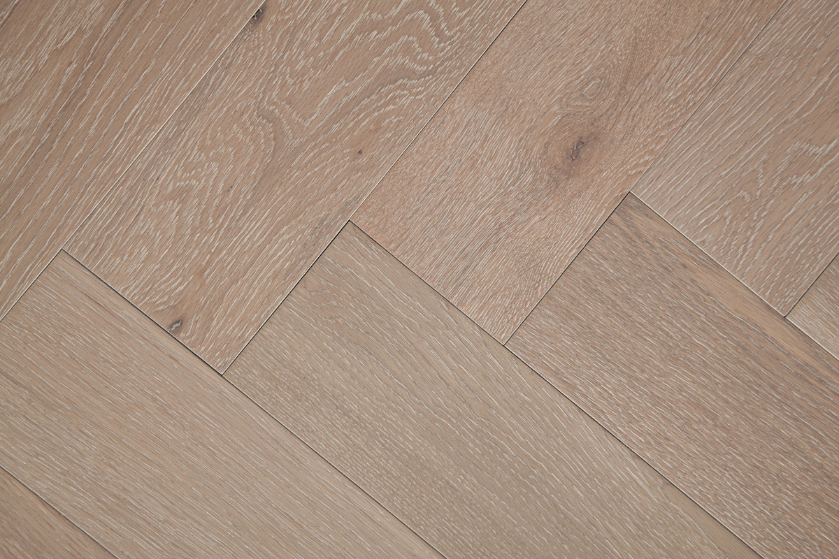 A photo showing Niagara herringbone oak hardwood from the Wildwood Nature Herringbone Collection. This hardwood has a very light grey-beige color with some white washing that accentuates the grain of the white oak. There is little to no variation and knotting in this wood, characteristic of its high grade.