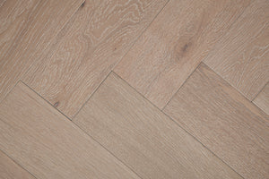 A photo showing Niagara herringbone oak hardwood from the Wildwood Nature Herringbone Collection. This hardwood has a very light grey-beige color with some white washing that accentuates the grain of the white oak. There is little to no variation and knotting in this wood, characteristic of its high grade.