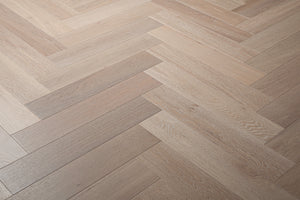 A photo showing Niagara herringbone oak hardwood from the Wildwood Nature Herringbone Collection. This hardwood has a very light grey-beige color with some white washing that accentuates the grain of the white oak. There is little to no variation and knotting in this wood, characteristic of its high grade.