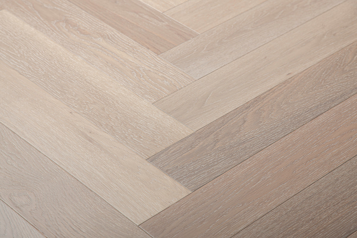 A photo showing Niagara herringbone oak hardwood from the Wildwood Nature Herringbone Collection. This hardwood has a very light grey-beige color with some white washing that accentuates the grain of the white oak. There is little to no variation and knotting in this wood, characteristic of its high grade.