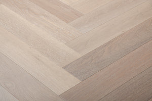 A photo showing Niagara herringbone oak hardwood from the Wildwood Nature Herringbone Collection. This hardwood has a very light grey-beige color with some white washing that accentuates the grain of the white oak. There is little to no variation and knotting in this wood, characteristic of its high grade.