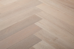 A photo showing Niagara herringbone oak hardwood from the Wildwood Nature Herringbone Collection. This hardwood has a very light grey-beige color with some white washing that accentuates the grain of the white oak. There is little to no variation and knotting in this wood, characteristic of its high grade.