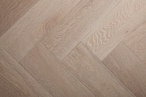 A photo showing Niagara herringbone oak hardwood from the Wildwood Nature Herringbone Collection. This hardwood has a very light grey-beige color with some white washing that accentuates the grain of the white oak. There is little to no variation and knotting in this wood, characteristic of its high grade.