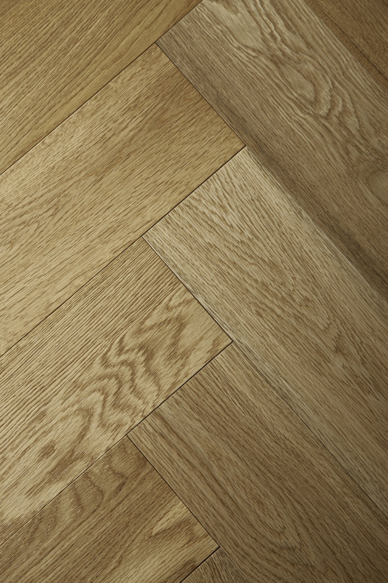 A photo showing the hardwood called oak natural herringbone, from the Wildwood Nature Herringbone Collection. This hardwood is the colour of natural oak, with a clear stain, showing the natural yellow and light amber hues of white oak. The high grade of the hardwood means there is minor variation from board to board and little to no knots in the wood.