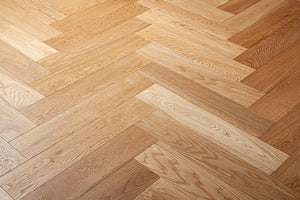 A photo showing the hardwood called oak natural herringbone, from the Wildwood Nature Herringbone Collection. This hardwood is the colour of natural oak, with a clear stain, showing the natural yellow and light amber hues of white oak. The high grade of the hardwood means there is minor variation from board to board and little to no knots in the wood.