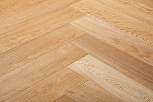 A photo showing the hardwood called oak natural herringbone, from the Wildwood Nature Herringbone Collection. This hardwood is the colour of natural oak, with a clear stain, showing the natural yellow and light amber hues of white oak. The high grade of the hardwood means there is minor variation from board to board and little to no knots in the wood.