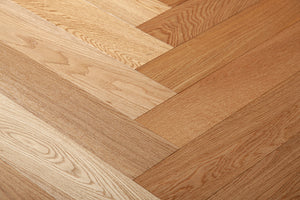 A photo showing the hardwood called oak natural herringbone, from the Wildwood Nature Herringbone Collection. This hardwood is the colour of natural oak, with a clear stain, showing the natural yellow and light amber hues of white oak. The high grade of the hardwood means there is minor variation from board to board and little to no knots in the wood.