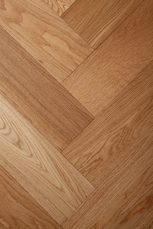 A photo showing the hardwood called oak natural herringbone, from the Wildwood Nature Herringbone Collection. This hardwood is the colour of natural oak, with a clear stain, showing the natural yellow and light amber hues of white oak. The high grade of the hardwood means there is minor variation from board to board and little to no knots in the wood.