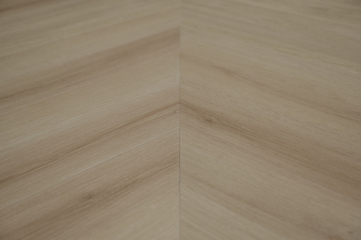 A picture showing the 6.5mm lvp flooring called Pompeii in the chevron pattern. This vinyl floor is uniquely crafted and can only be installed in the chevron pattern. It has a light medium beige hue and silver chain embossing, giving the floor an ultra-realistic look.