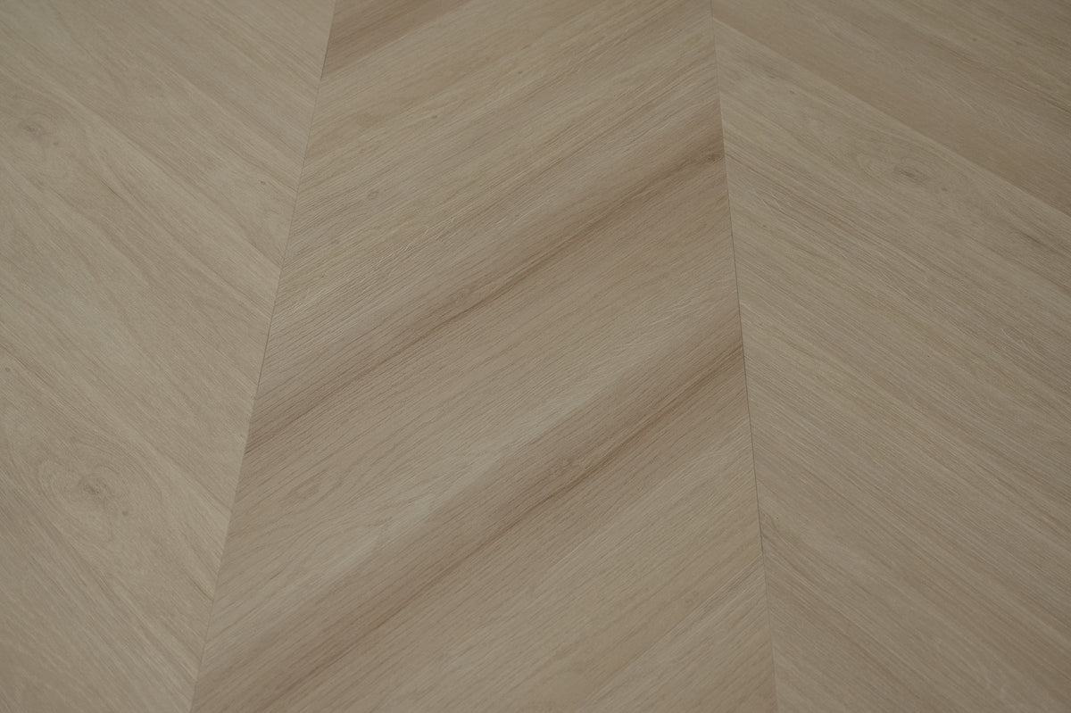 A picture showing the 6.5mm lvp flooring called Pompeii in the chevron pattern. This vinyl floor is uniquely crafted and can only be installed in the chevron pattern. It has a light medium beige hue and silver chain embossing, giving the floor an ultra-realistic look.