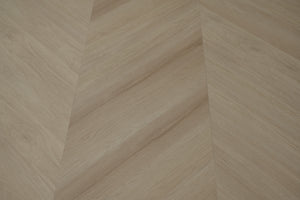 A picture showing the 6.5mm lvp flooring called Pompeii in the chevron pattern. This vinyl floor is uniquely crafted and can only be installed in the chevron pattern. It has a light medium beige hue and silver chain embossing, giving the floor an ultra-realistic look.