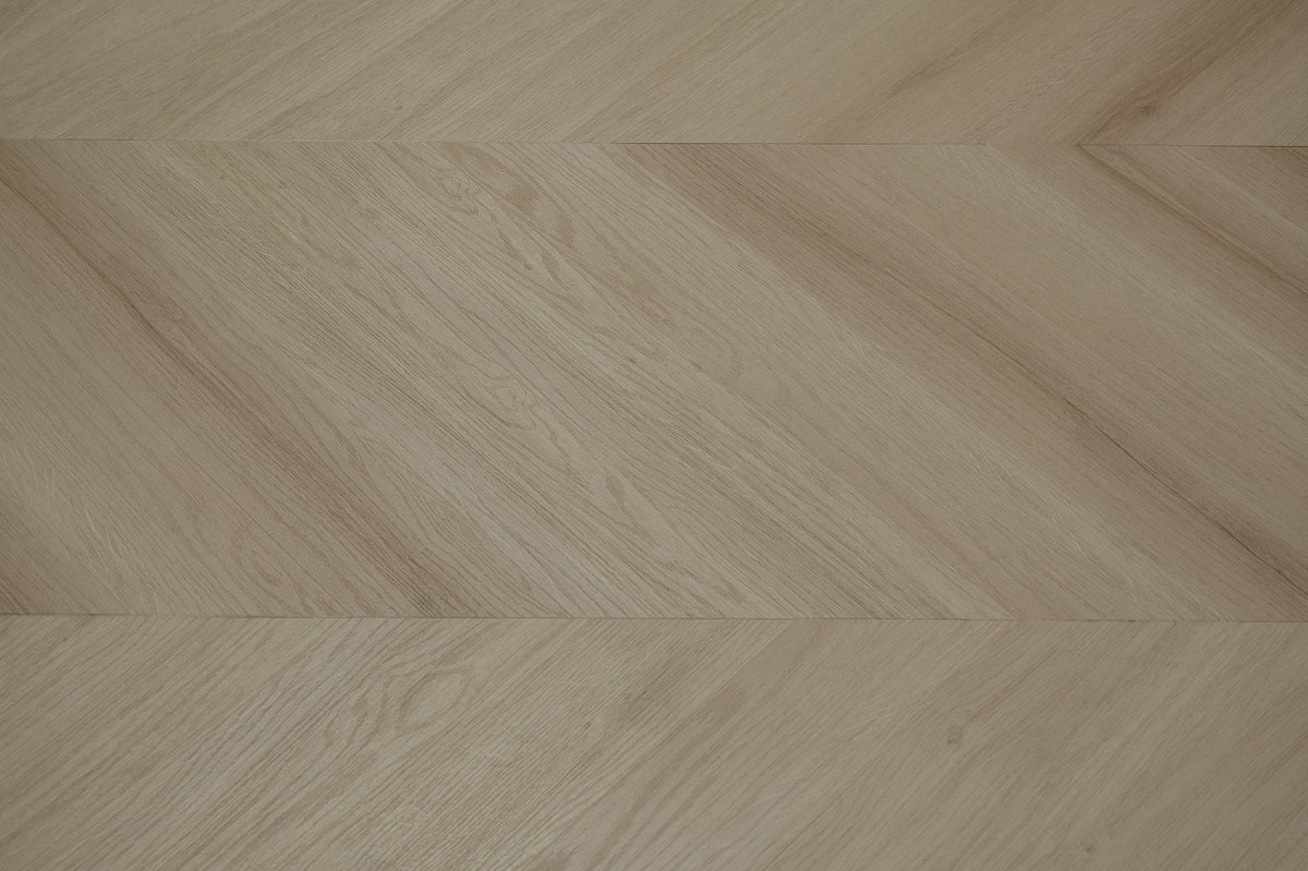 A picture showing the 6.5mm lvp flooring called Pompeii in the chevron pattern. This vinyl floor is uniquely crafted and can only be installed in the chevron pattern. It has a light medium beige hue and silver chain embossing, giving the floor an ultra-realistic look.