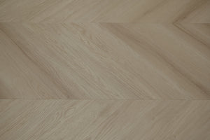 A picture showing the 6.5mm lvp flooring called Pompeii in the chevron pattern. This vinyl floor is uniquely crafted and can only be installed in the chevron pattern. It has a light medium beige hue and silver chain embossing, giving the floor an ultra-realistic look.